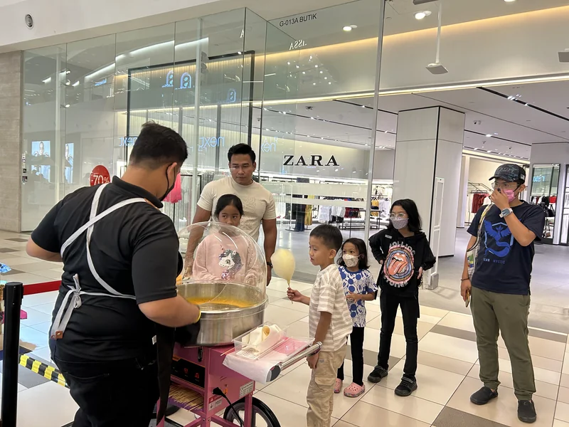 An operator making candy floss in the pink trolley machine as families watch at MyTOWN