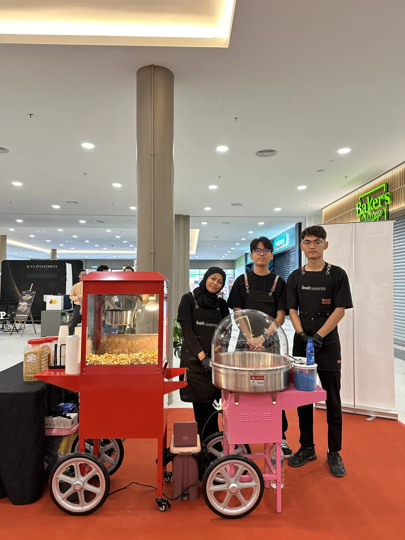 Three event crew with the red popcorn trolley and pink candy-floss machine at Bites