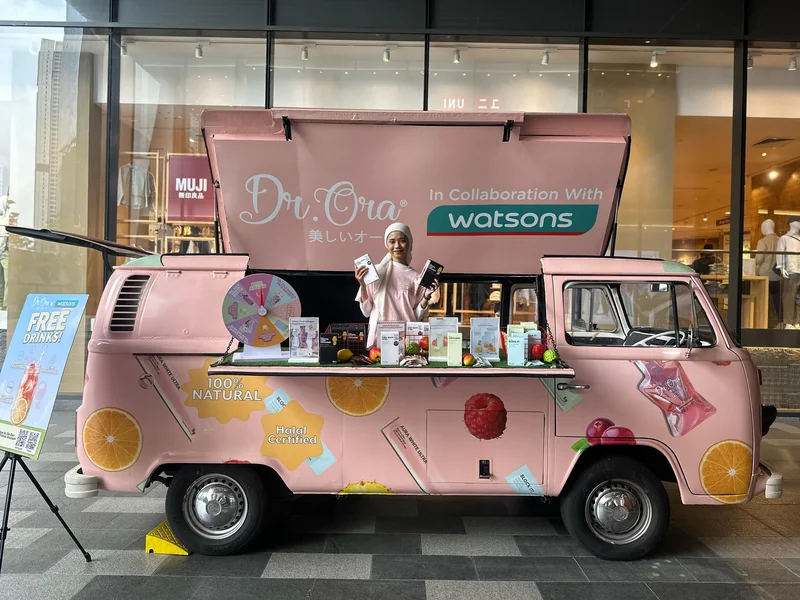 A pink Dr. Oria and Watsons-branded Kombi with an open serving hatch at an event