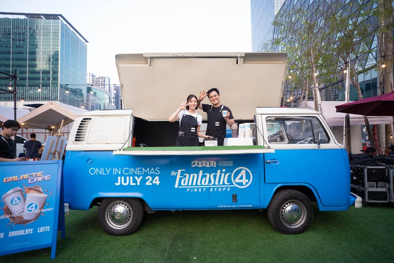 Two crew behind the open serving hatch of a blue Fantastic Four-branded Kombi