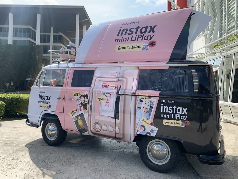 A pink instax mini LiPlay-branded Kombi with a raised display hatch at an outdoor activation