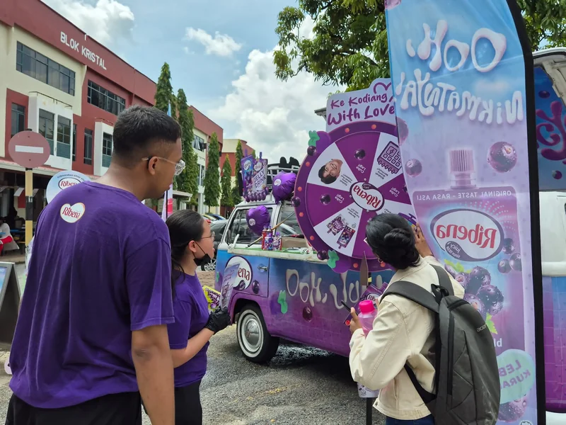 A guest and crew at a prize wheel beside the Ribena Kombi