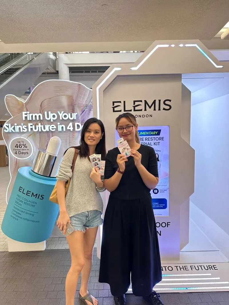 Two guests holding photo strips beside the Elemis photobooth
