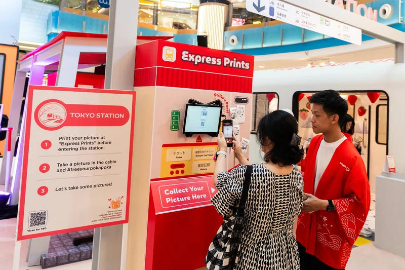 A guest and POKKA crew member at the red-and-cream Express Prints receipt photobooth