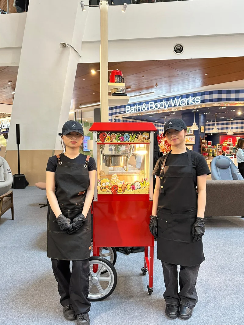 Two event crew beside the red popcorn machine and wheeled trolley at Coway Innovation Fest
