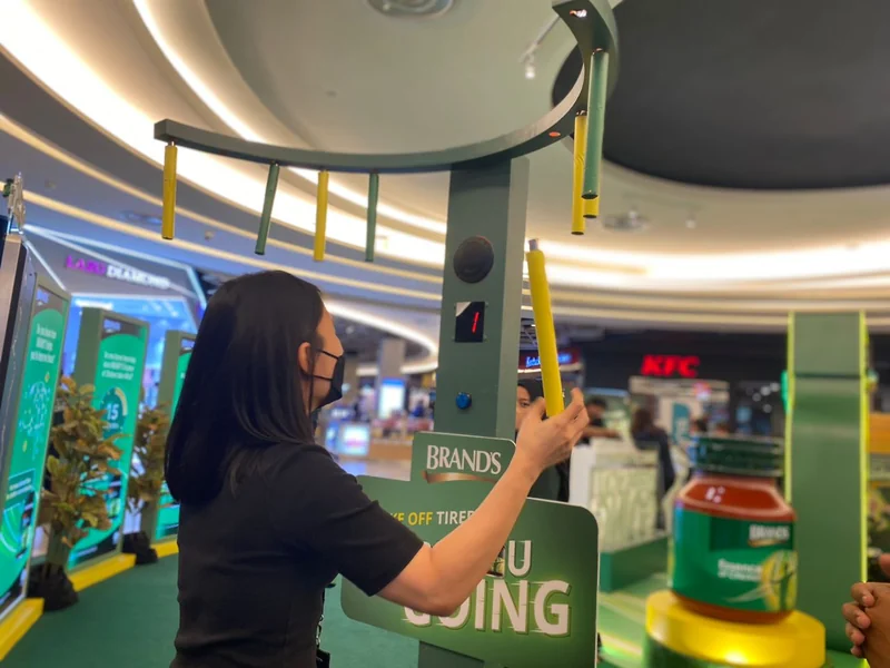 A participant beneath the green overhead ring with yellow hanging sticks at a BRAND’S activation