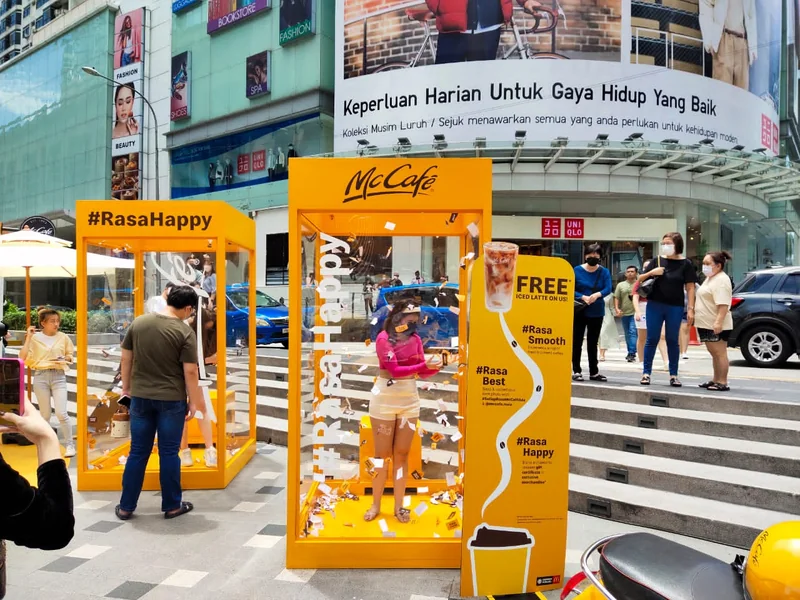 A participant catching vouchers in the yellow McCafé wind chamber with guests beside the game