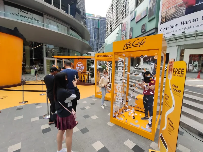 A participant catching vouchers in a yellow McCafé wind chamber as guests watch